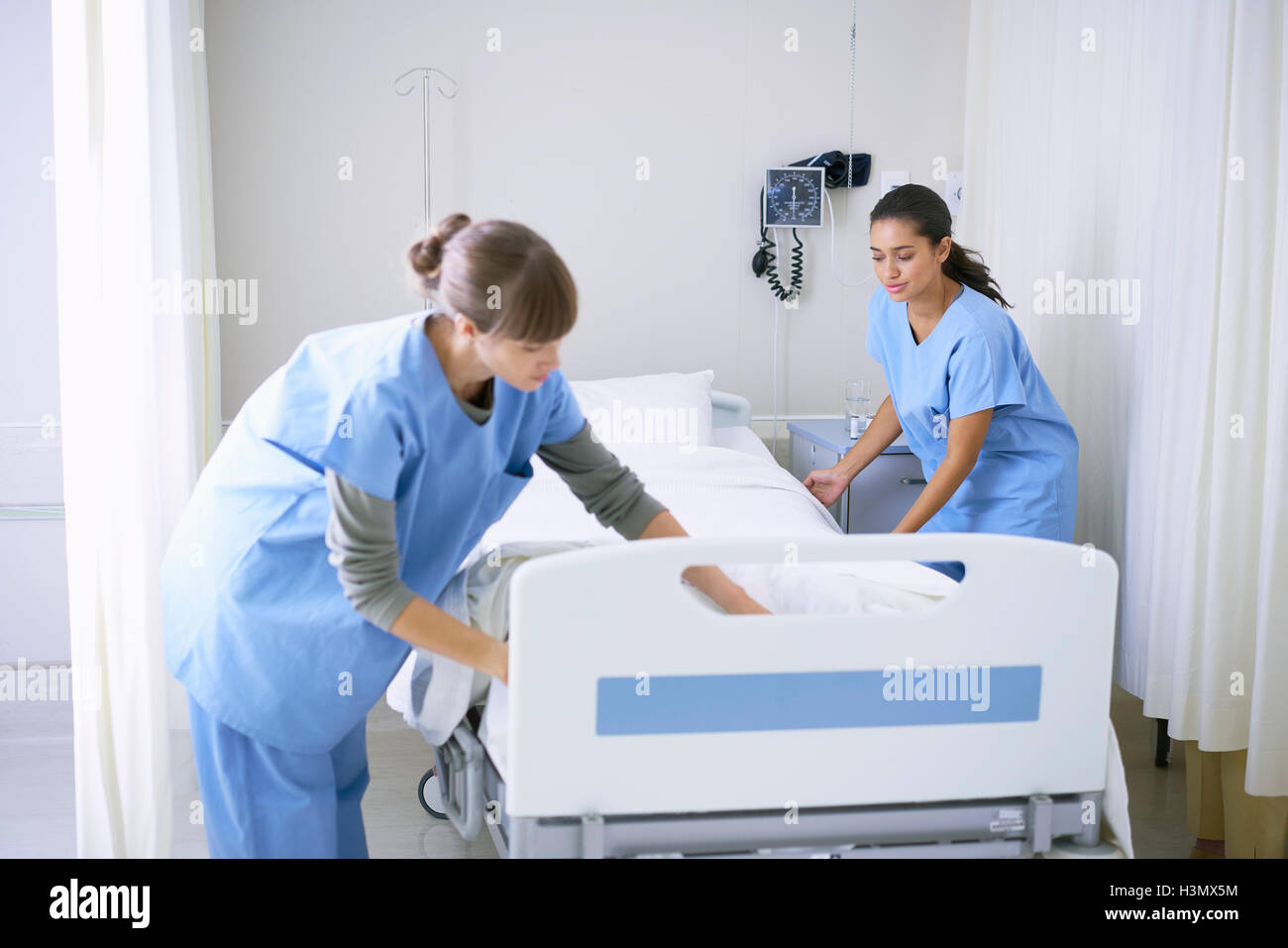 Two female nurses making hospital bed in ward Stock Photo
