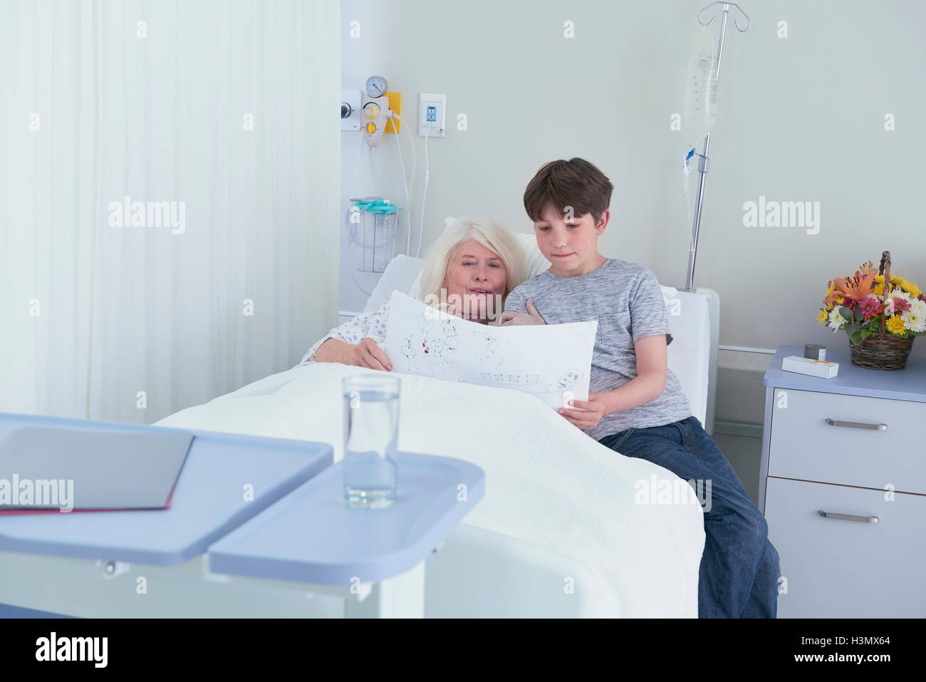 Senior female patient in hospital bed looking at grandson's drawing Stock Photo