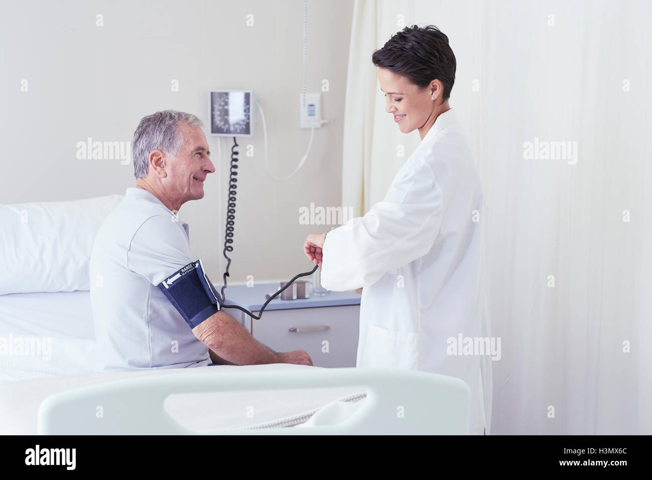 Female doctor using blood pressure gauge and timing pulse of senior male patient Stock Photo