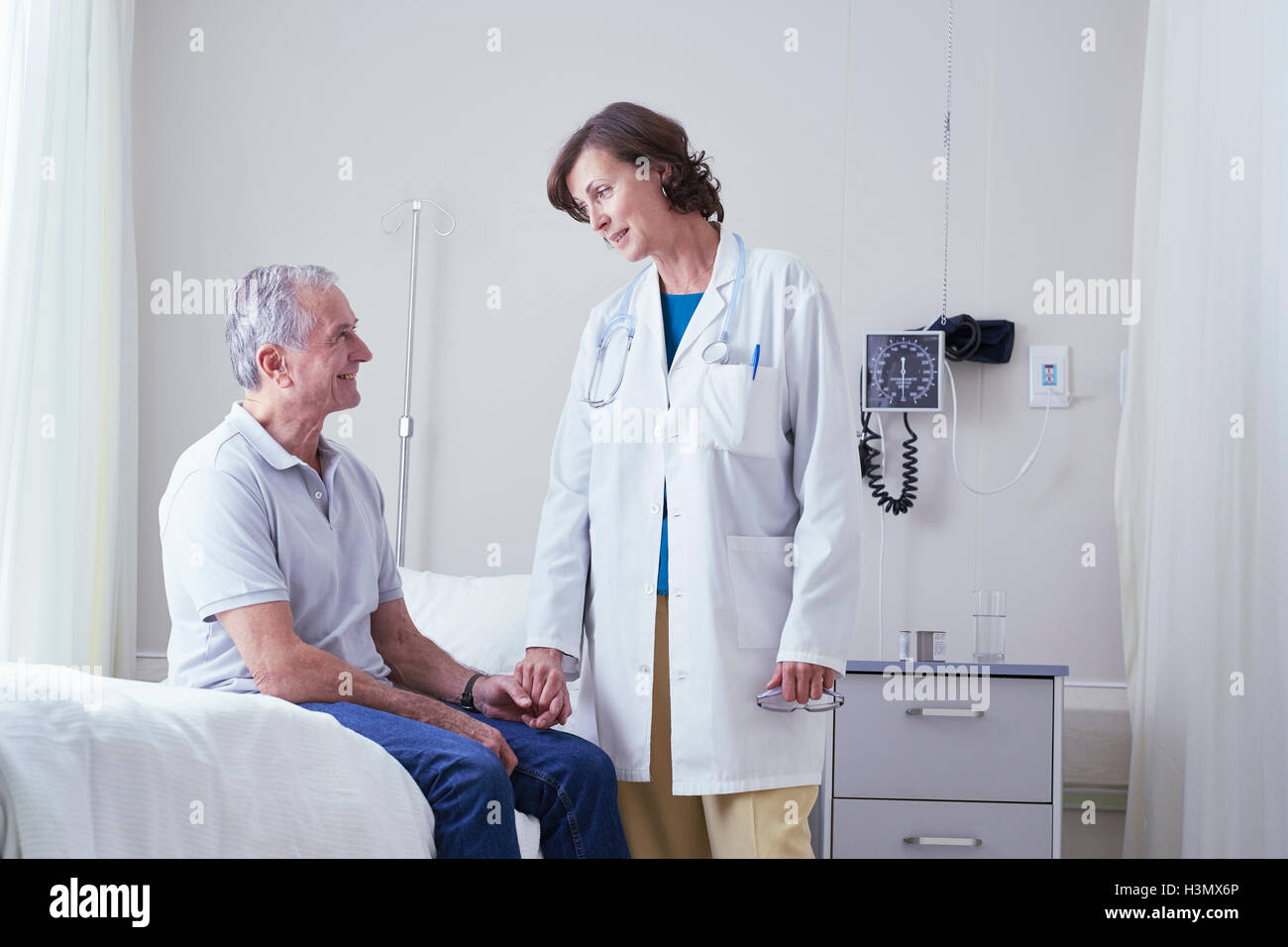 Female doctors explaining to senior male patient on hospital bed Stock Photo