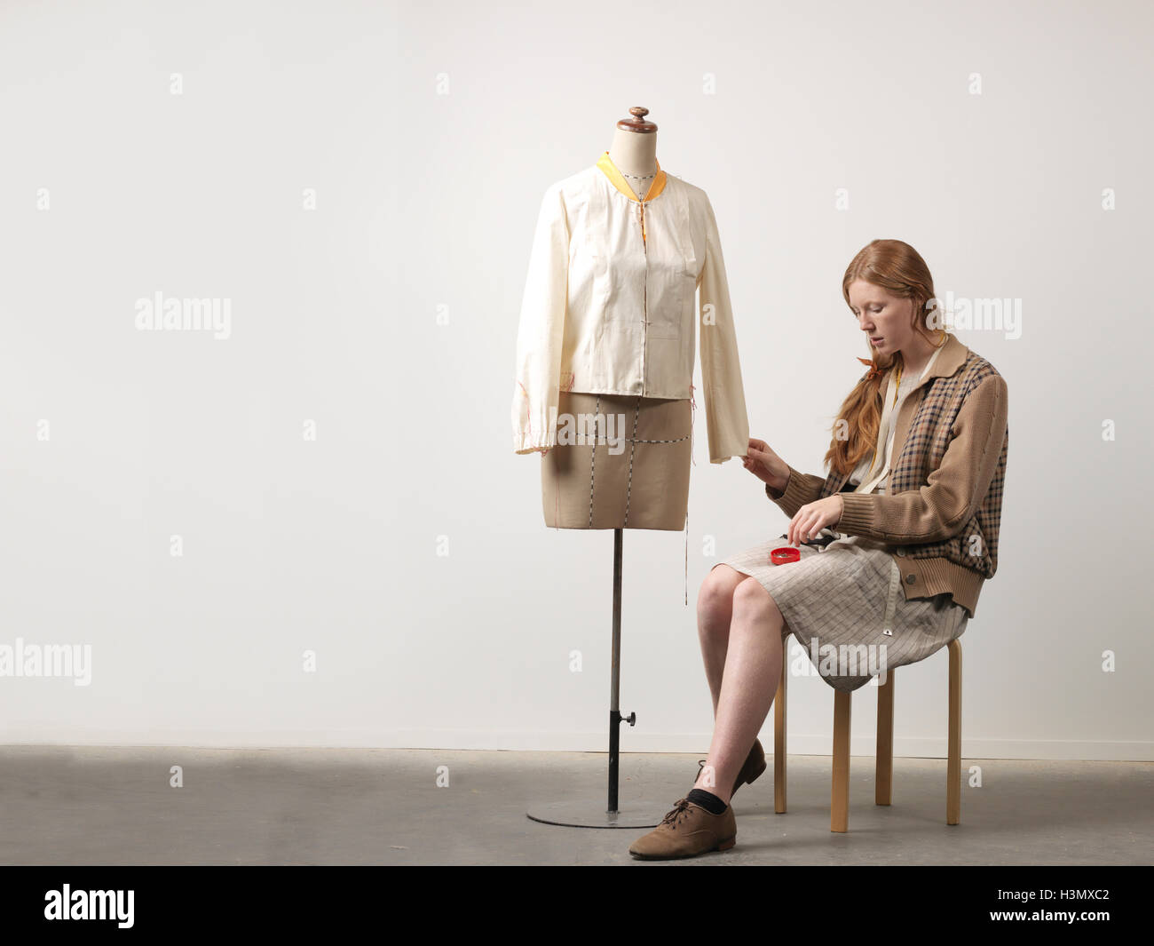Young female fashion designer sitting on stool pinning blouse on dressmaker's dummy Stock Photo