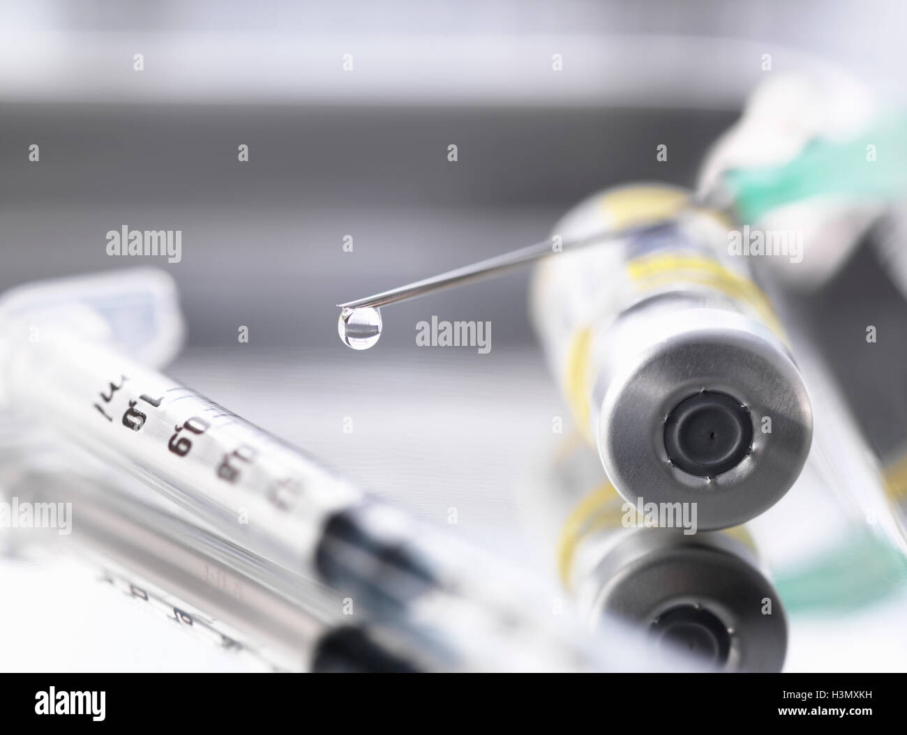 Ampoule containing a drug dose next to a syringe with a droplet of medicine at the end of the needle Stock Photo