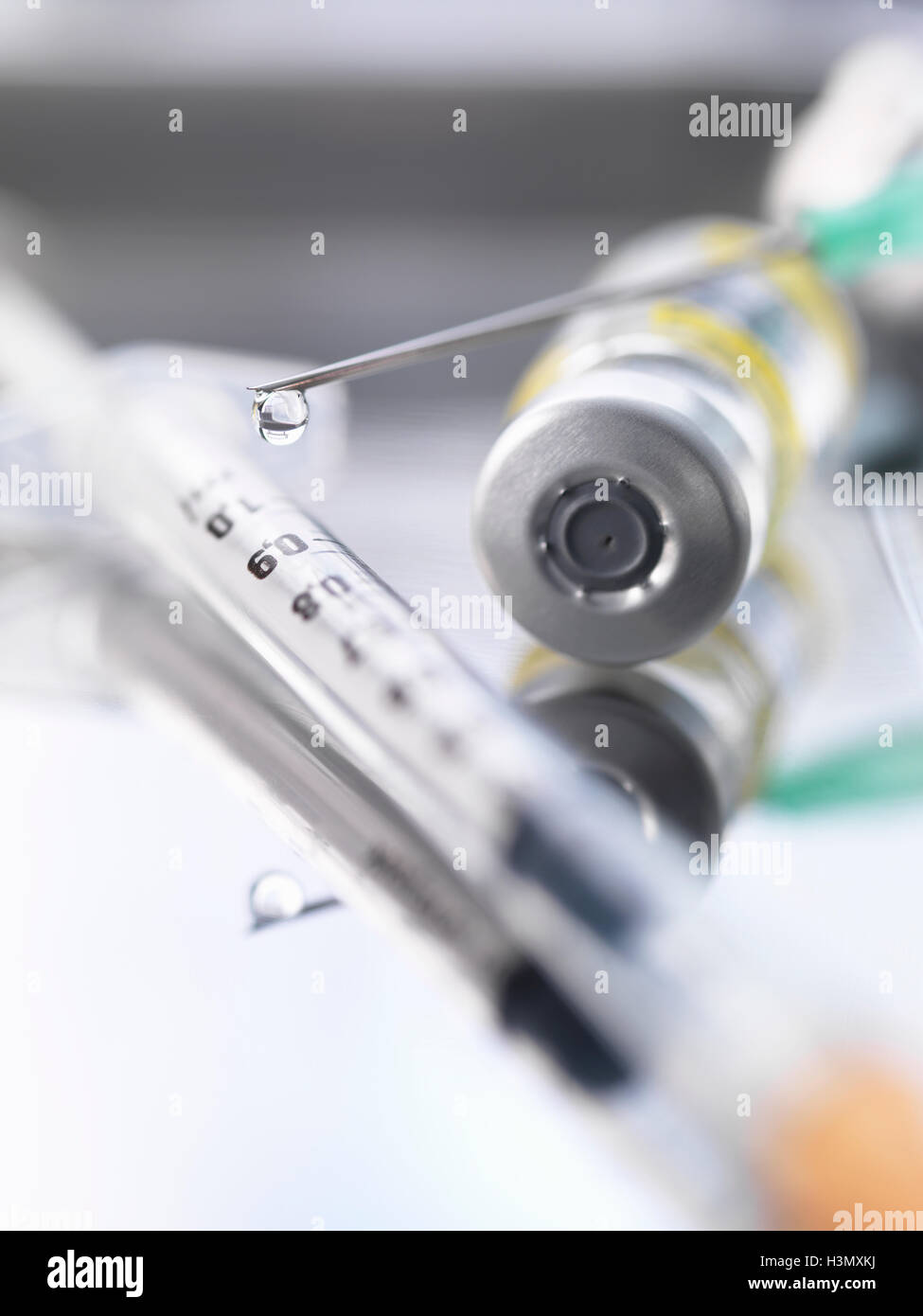 Ampoule containing a drug dose next to a syringe with a droplet of medicine at the end of the needle Stock Photo