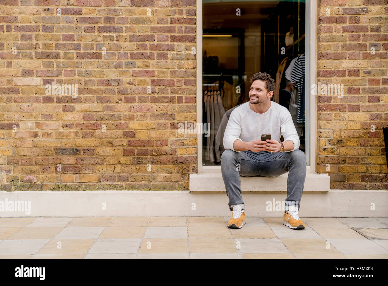 Young man with smartphone sitting on doorstep, Kings Road, London, UK Stock Photo