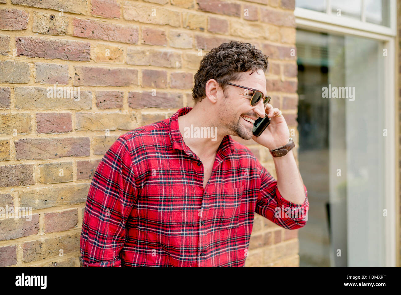 Young man in front of brick wall talking on smartphone Stock Photo
