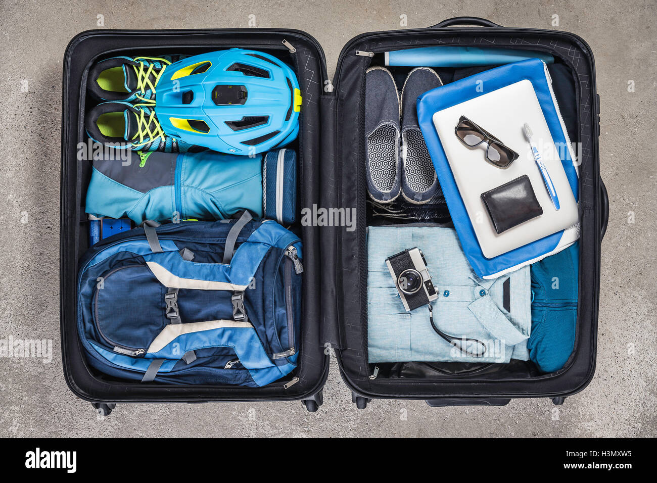 Overhead view of open packed suitcase with blue shirt, bike helmet, backpack, retro camera and toothbrush Stock Photo