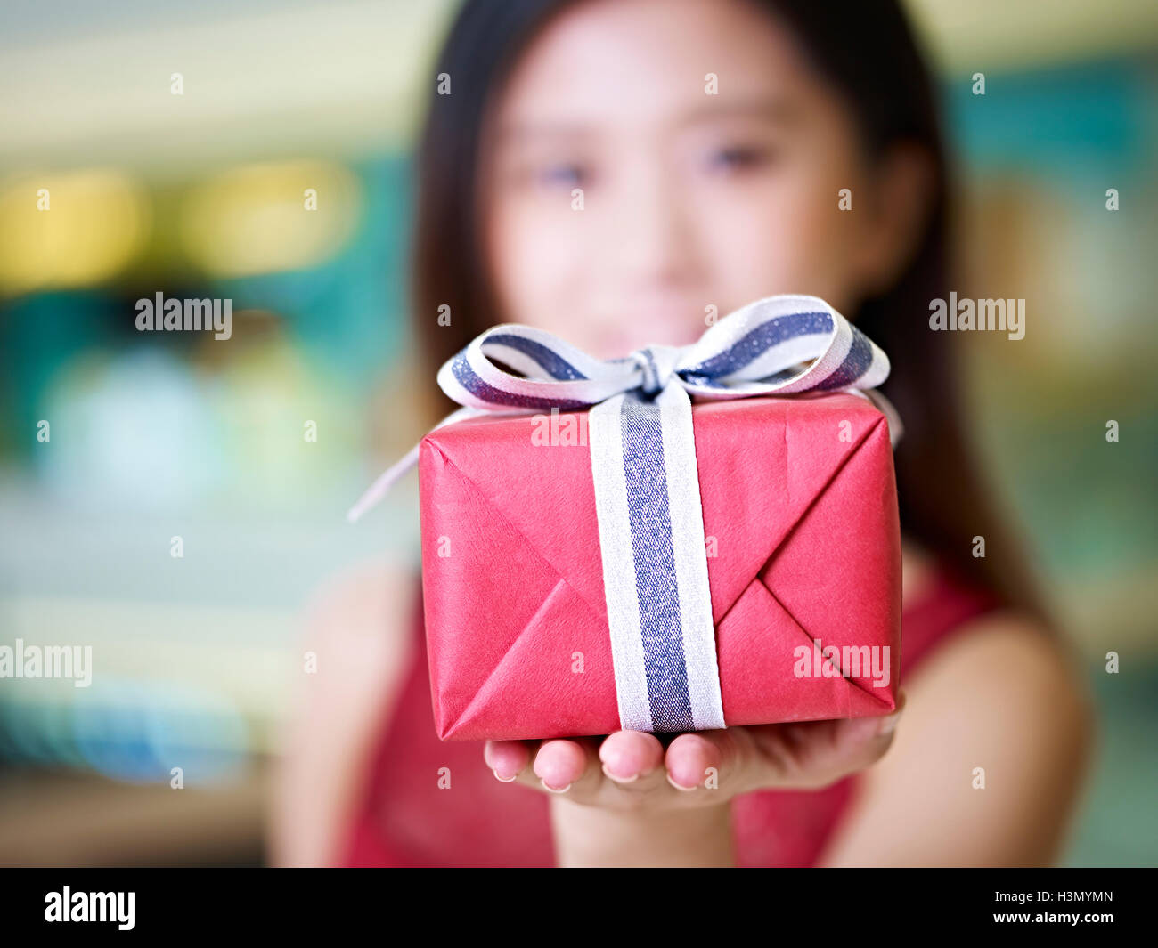 beautiful young asian woman presenting a wrapped box of gift and smiling, selective focus on the box Stock Photo