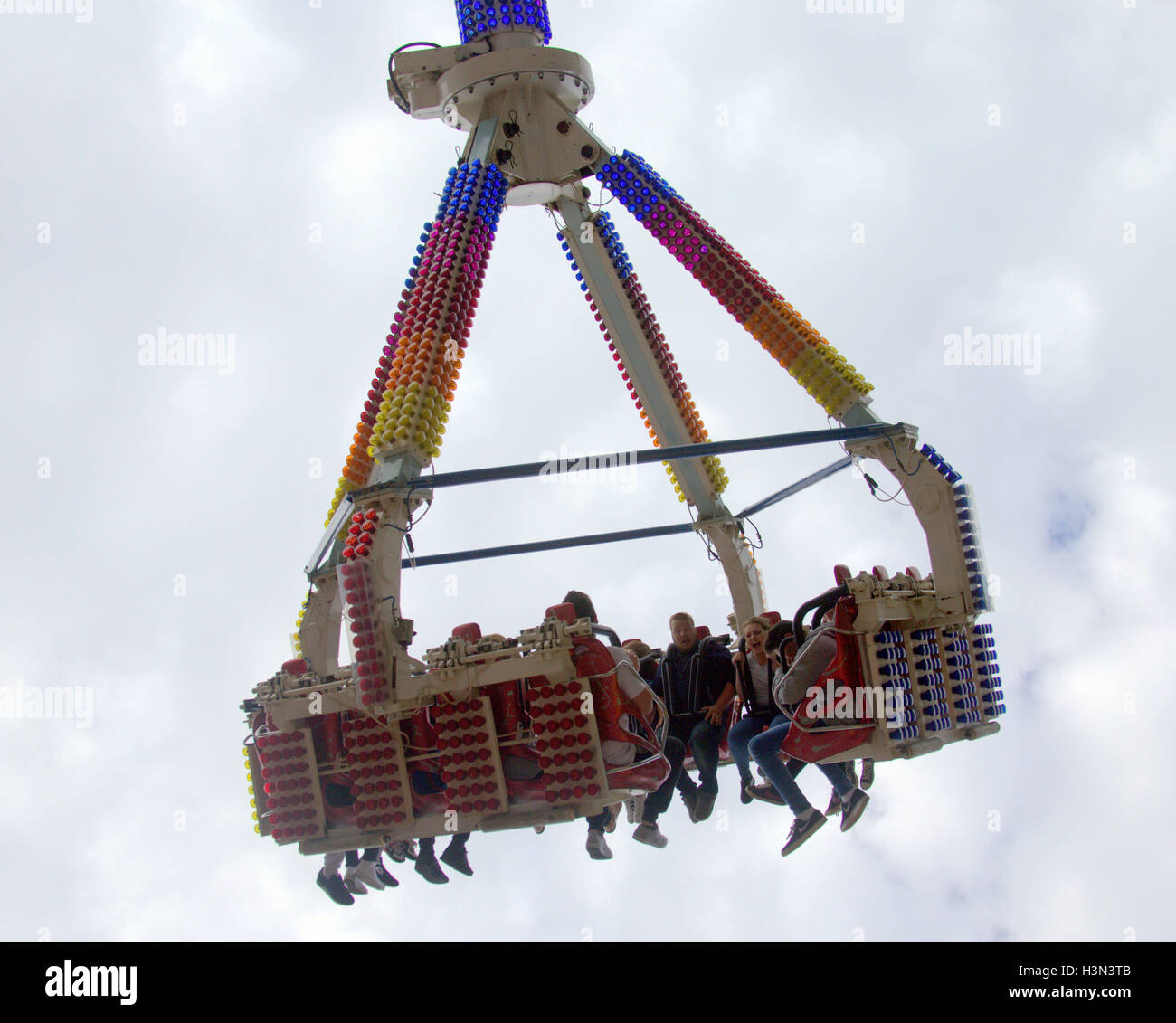 fairground ride with people boys and girls being lifted and spun on an arm of a ride high in the sky with cloud background Stock Photo