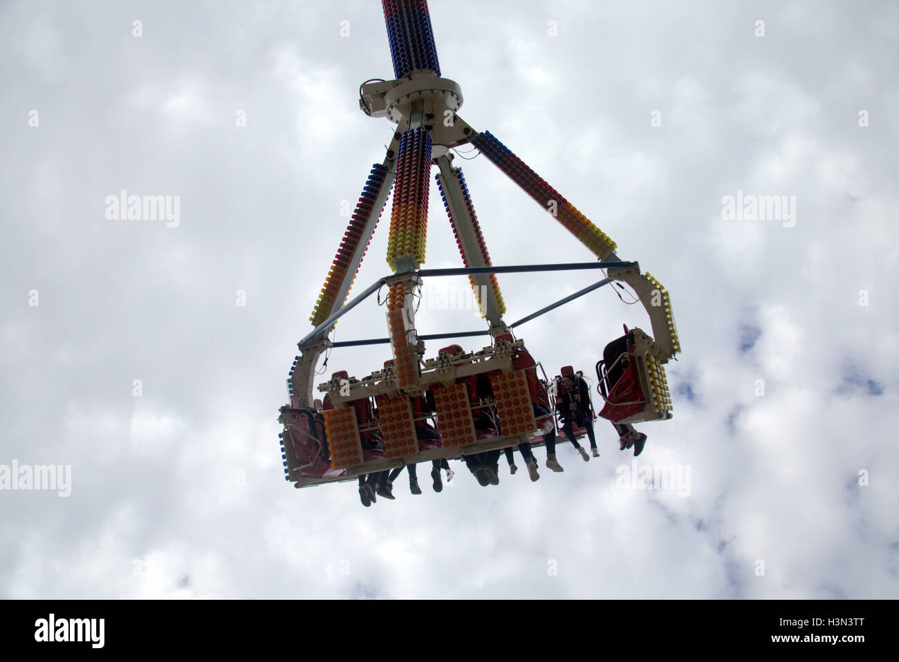 fairground ride with people boys and girls being lifted and spun on an arm of a ride high in the sky with cloud background Stock Photo
