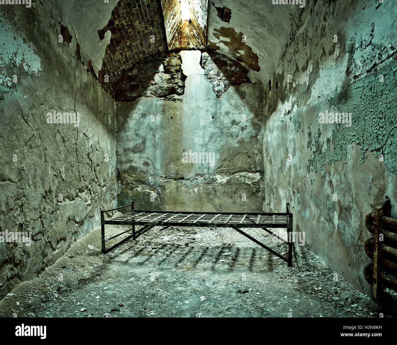 Crumbling abandoned prison cell with cot Stock Photo