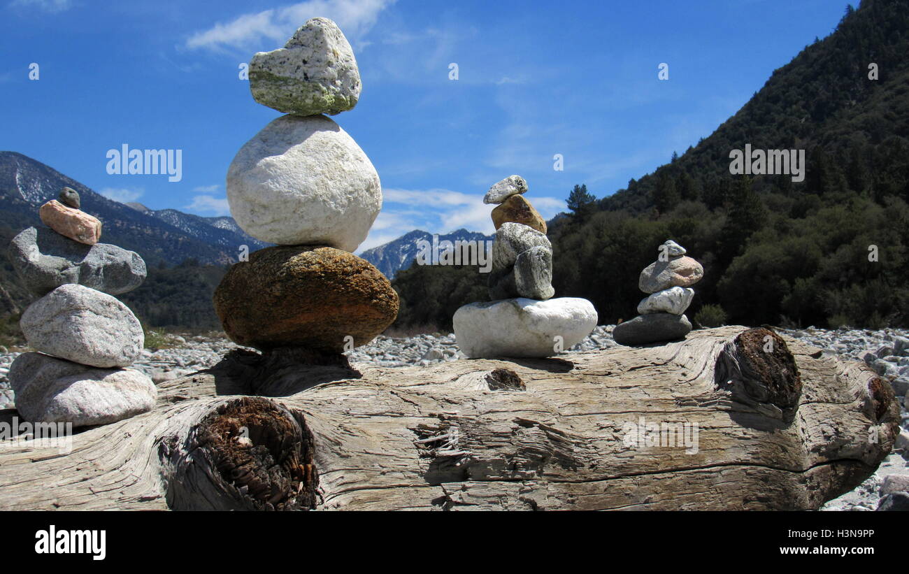 Stone pile cairns in riverbed balancing on a driftwood log with mountains in the background Stock Photo