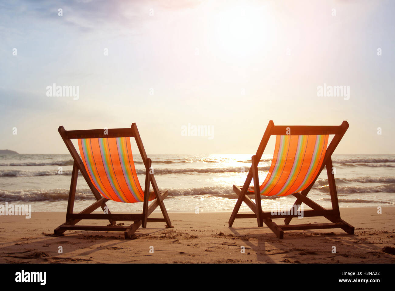 Two deckchairs on the beach with bright sun and waves Stock Photo