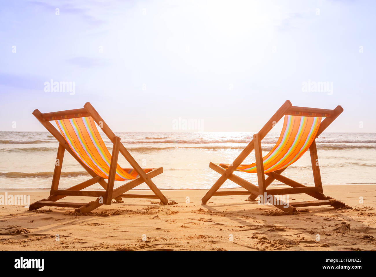 Two deckchairs on the beach at sunset with a tropical sea background Stock Photo
