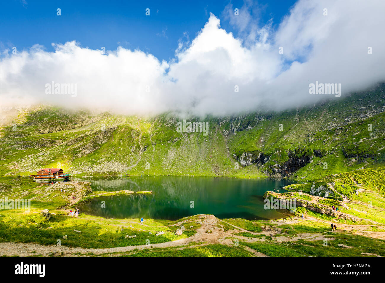 Balea lake and chalet in Fagaras mountains, Romania. Unidentifiable tourists enjoy the scenery. Stock Photo