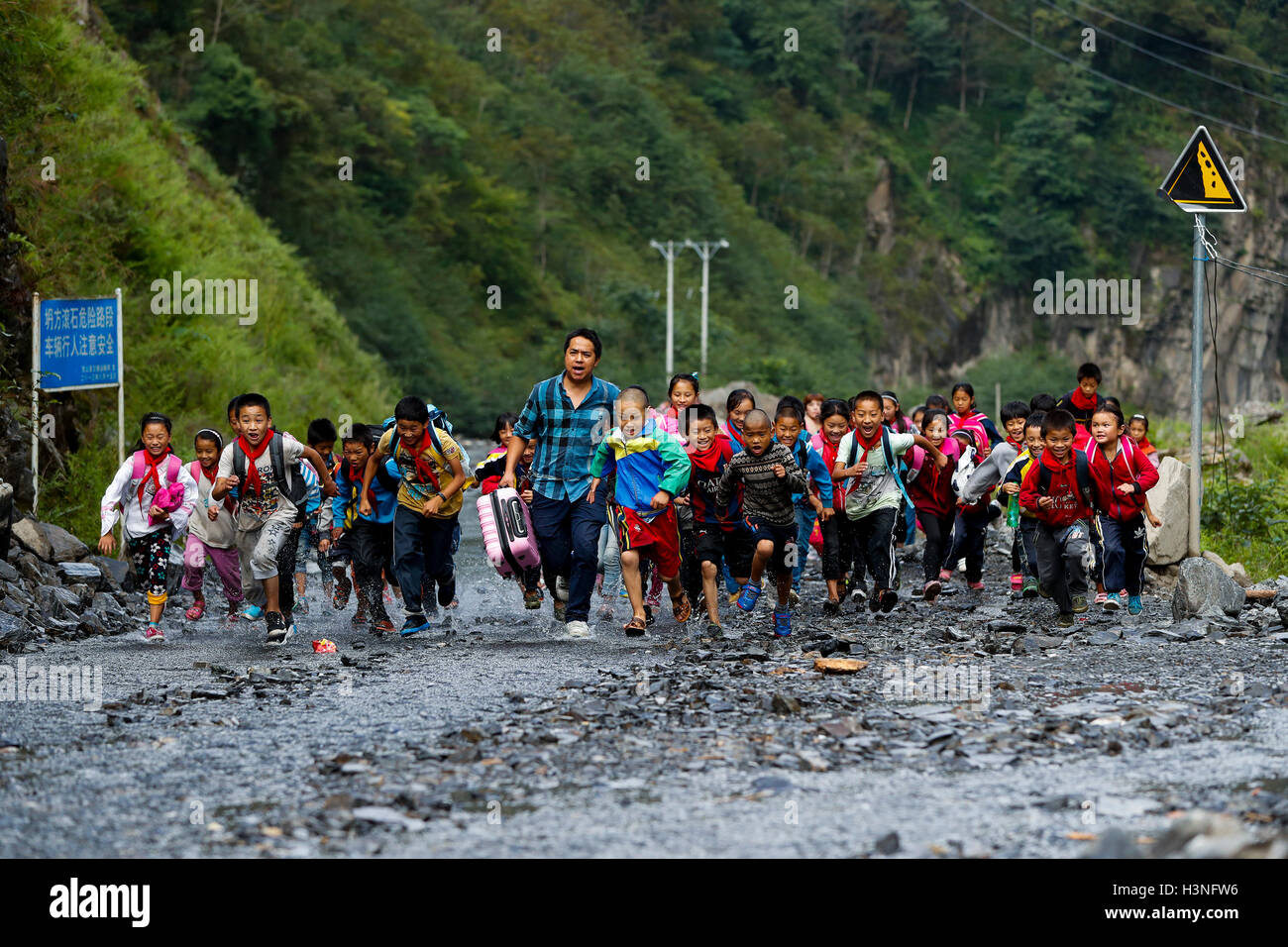 (161011) -- BEIJING, Oct. 11, 2016 (Xinhua) -- Photo taken on Sept. 28, 2016 shows Sang Lei and students running on a flooded road to Dimaluo Village, a remote village in Nujiang Lisu Autonomous Prefecture of southwest China's Yunnan Province. Sang Lei, a college graduate majored in computer education, has been as a voluntary teacher of Pengdang Primary School since 2007. In nearly ten years of teaching, he tried his best to provide better learning environment for his pupils. Since 2006, more than 500,000 young people in China like Sang Lei have gone to central and western China to offer educ Stock Photo
