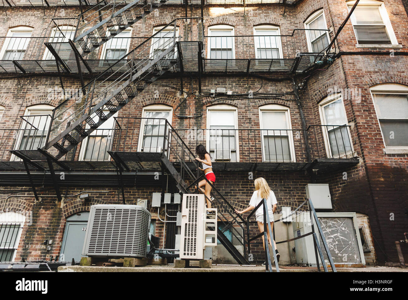 Women climbing fire escape ladder of apartment building, Boston