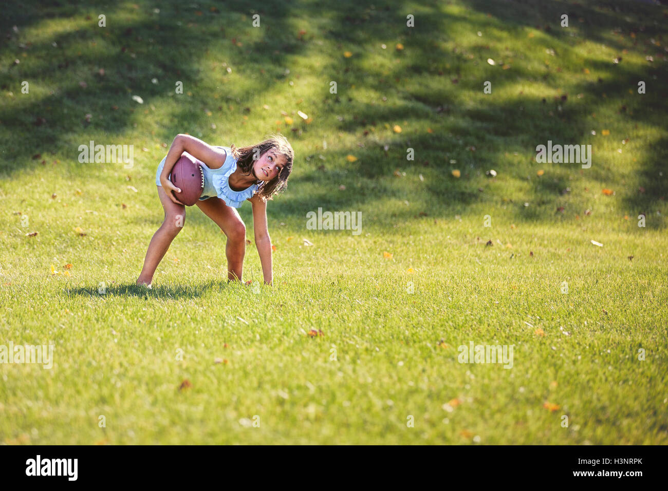 Girl bending forward playing American football in park Stock Photo