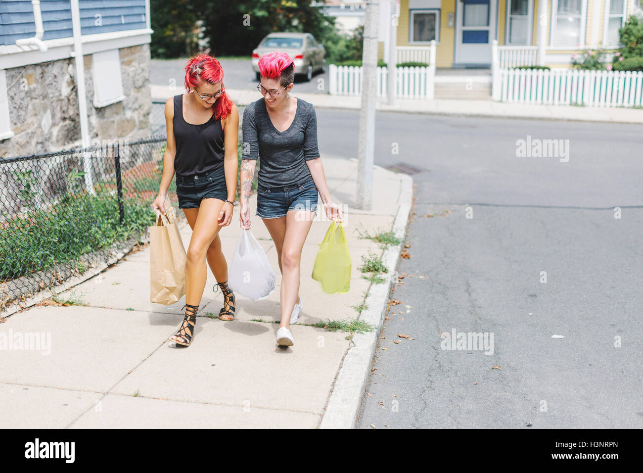 Two female friends with pink hair walking on sidewalk carrying shopping bags Stock Photo