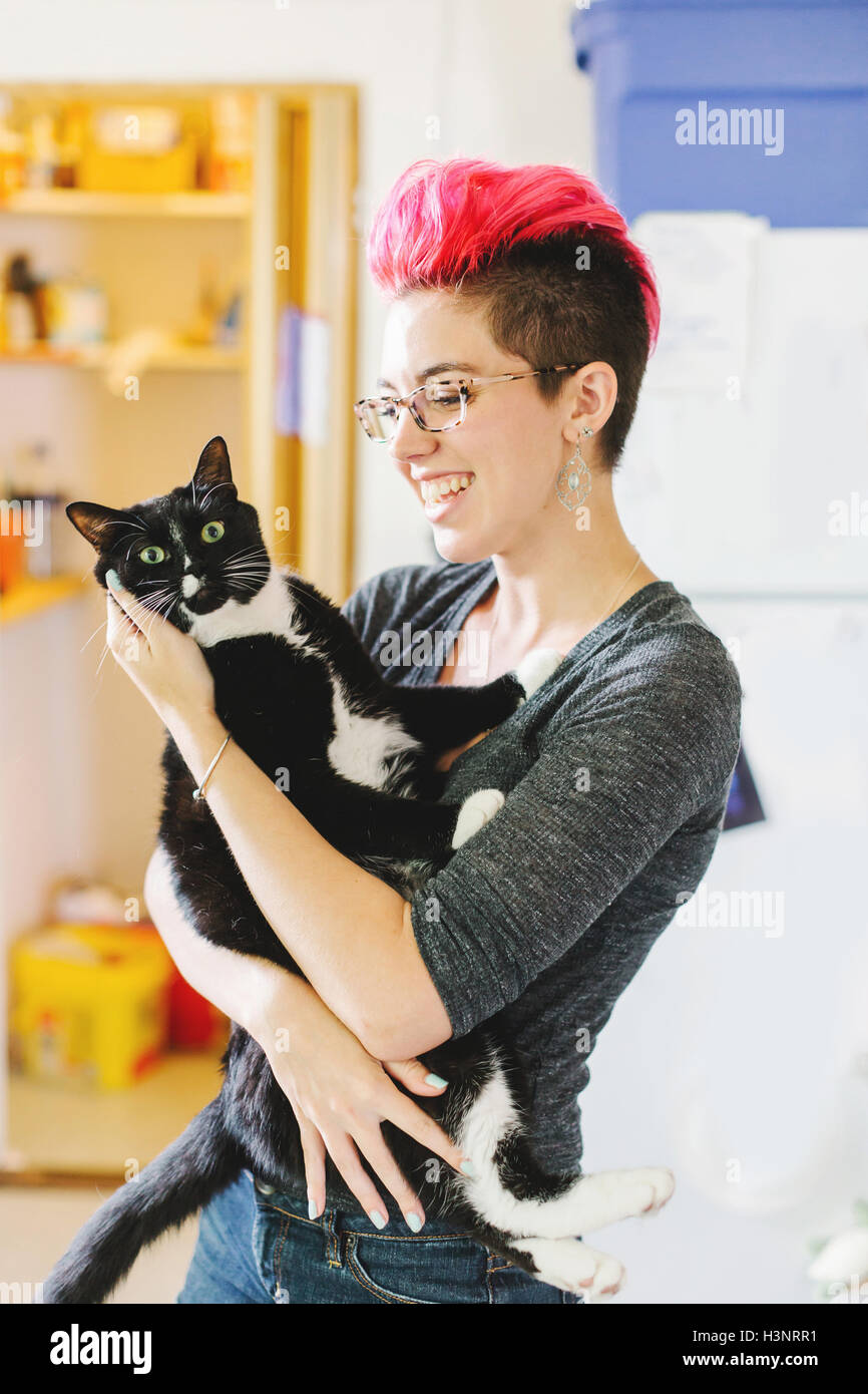 Young woman with pink carrying wide-eyed cat in kitchen Stock Photo