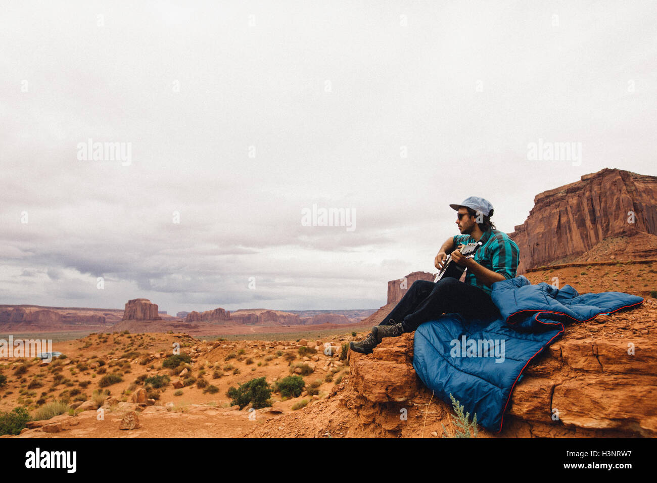 Young man sitting on rock playing acoustic guitar, Monument Valley, Arizona, USA Stock Photo
