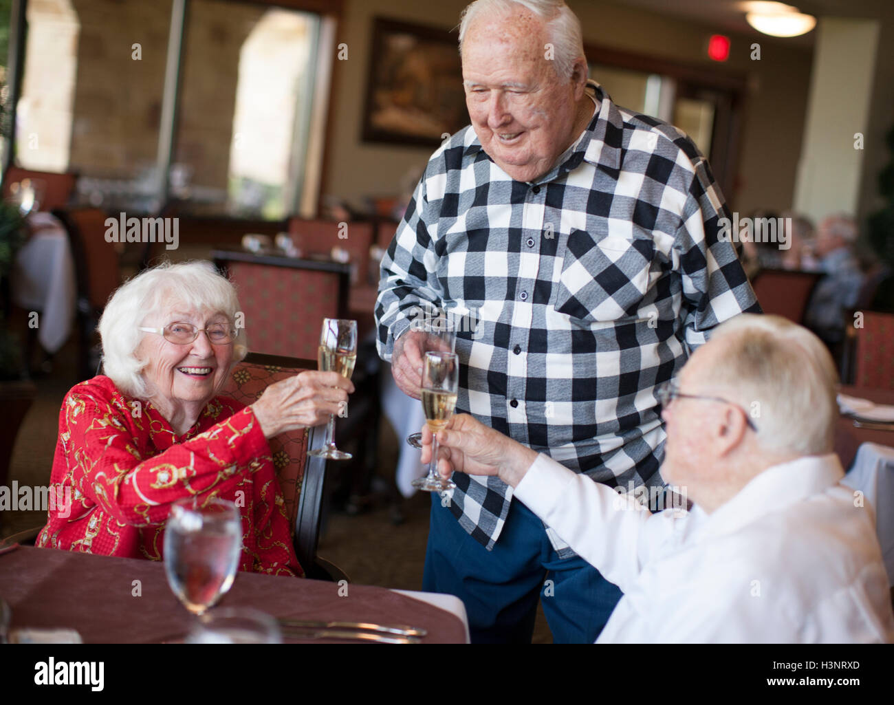 Three senior adults in restaurant, holding champagne glasses, making toast Stock Photo