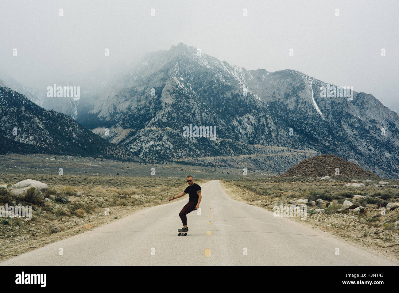 Man skateboarding on road by mountains, Lone Pine, California, USA Stock Photo