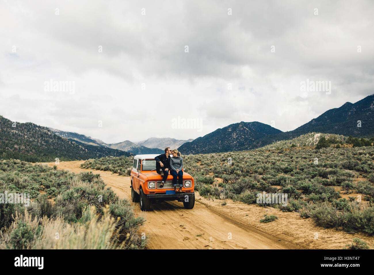 Couple sitting on vehicle in scrubland by mountains, Kennedy Meadows, California, USA Stock Photo