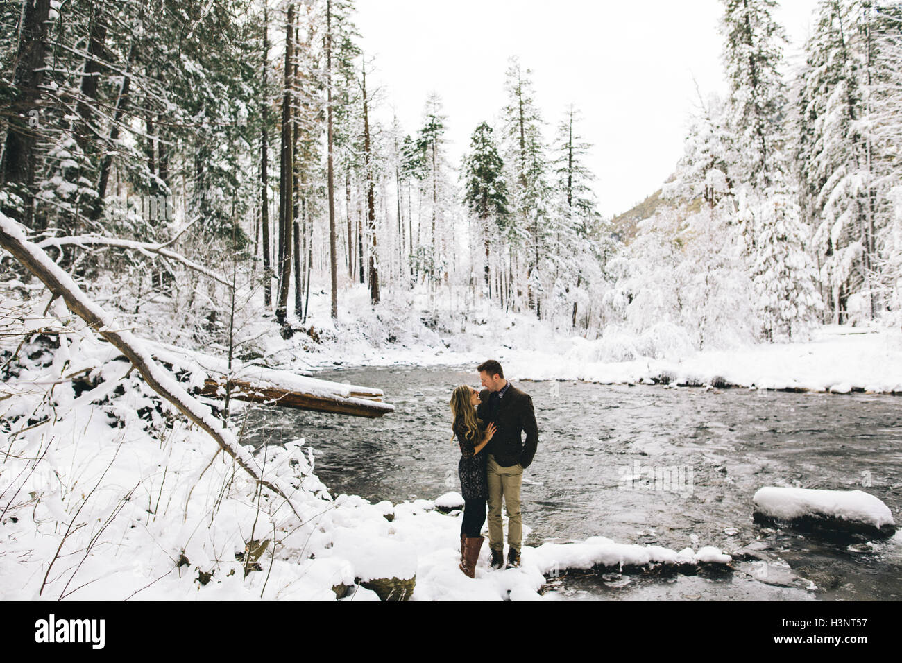 Couple in snow-covered forest by river face to face smiling Stock Photo