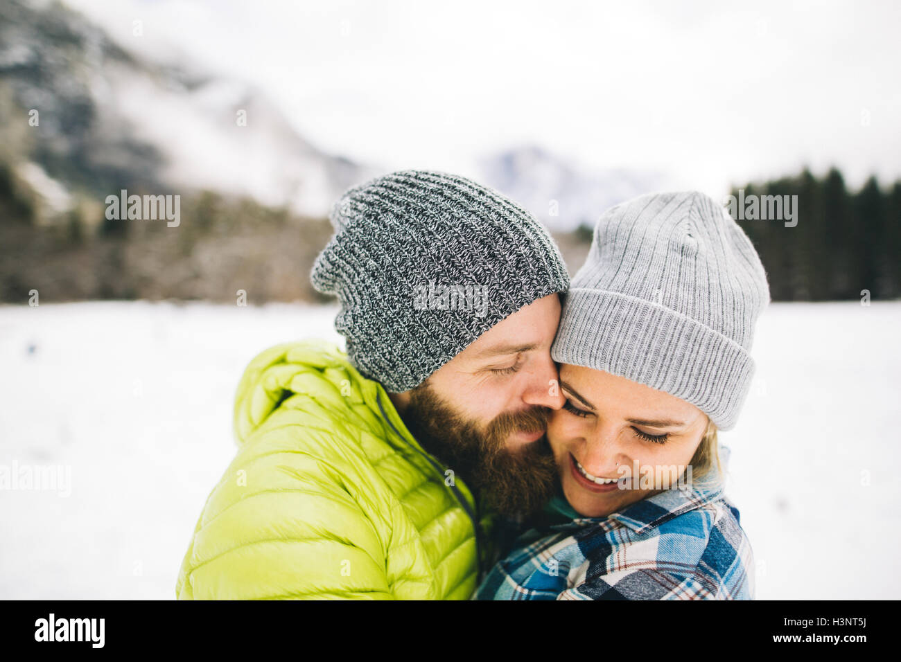 Couple on snow-covered landscape wearing knit hats hugging Stock Photo