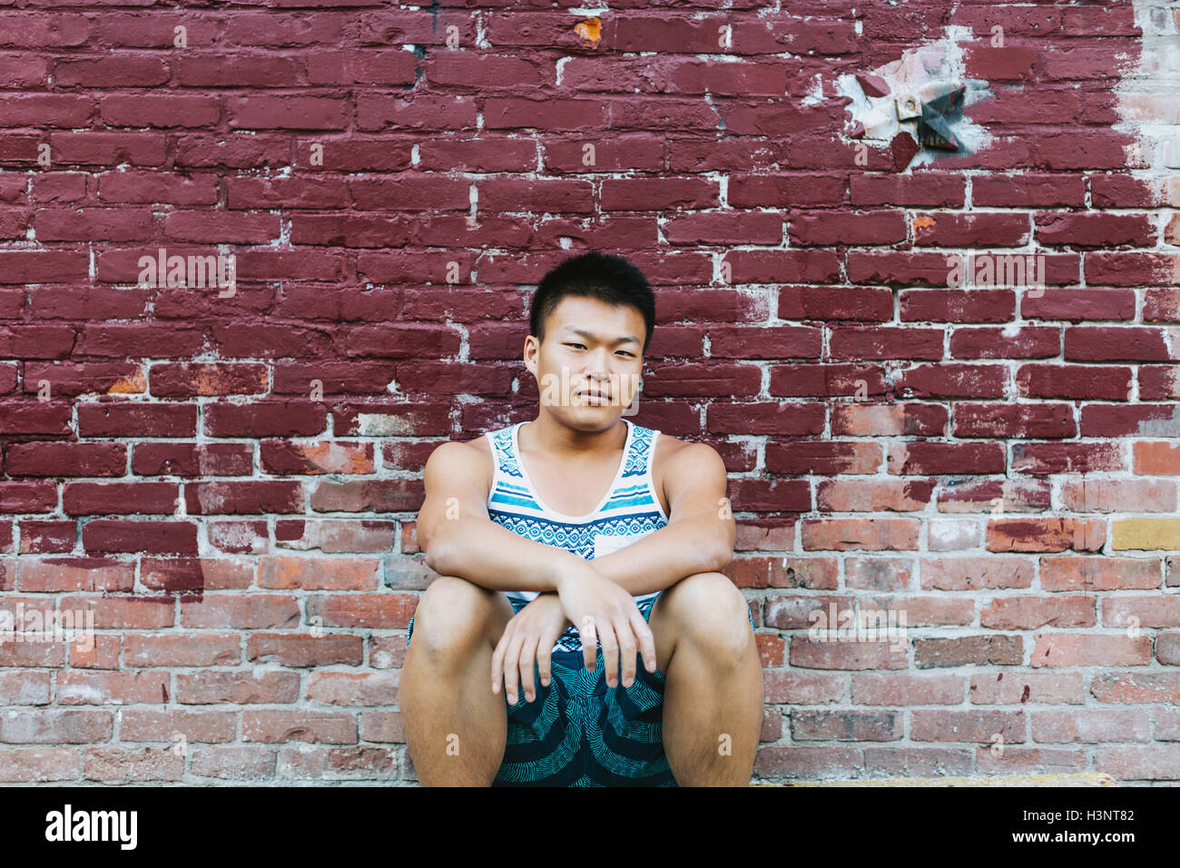 Man squatting in front of brick wall Stock Photo