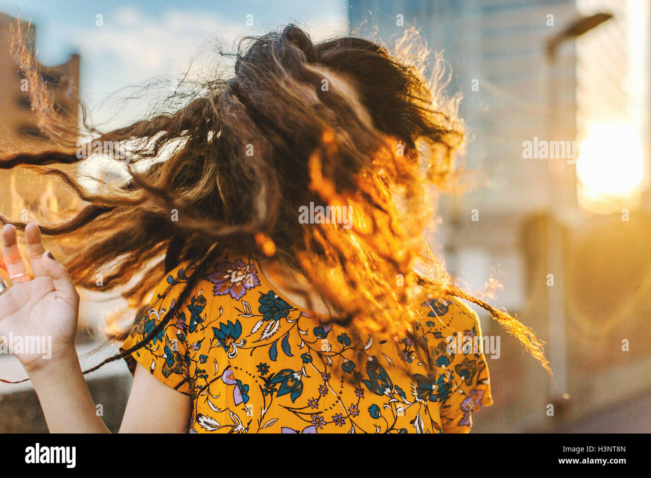 Front view of young woman shaking her long wavy hair in city sunlight Stock Photo