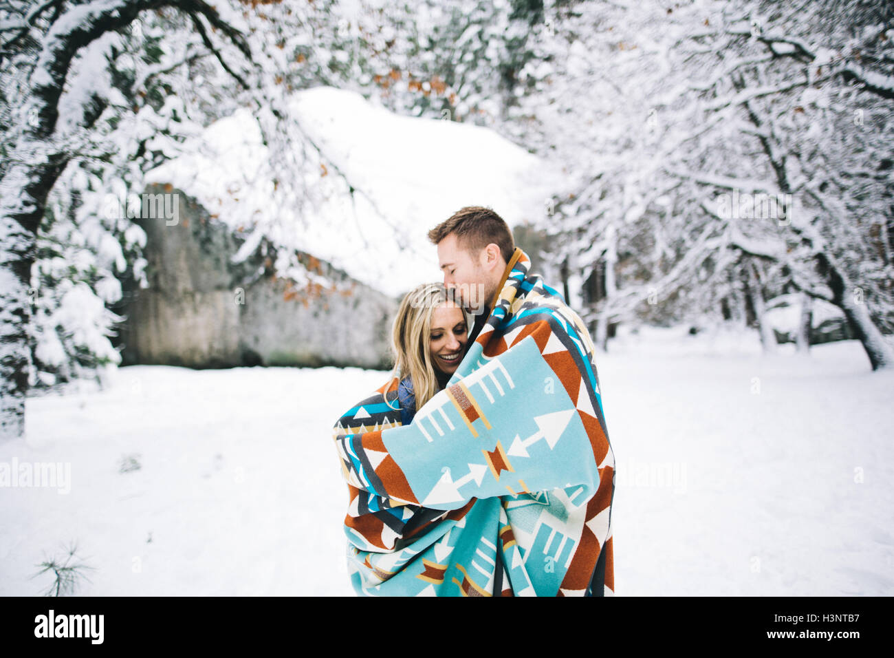 Couple in snow-covered forest wrapped in blanket Stock Photo