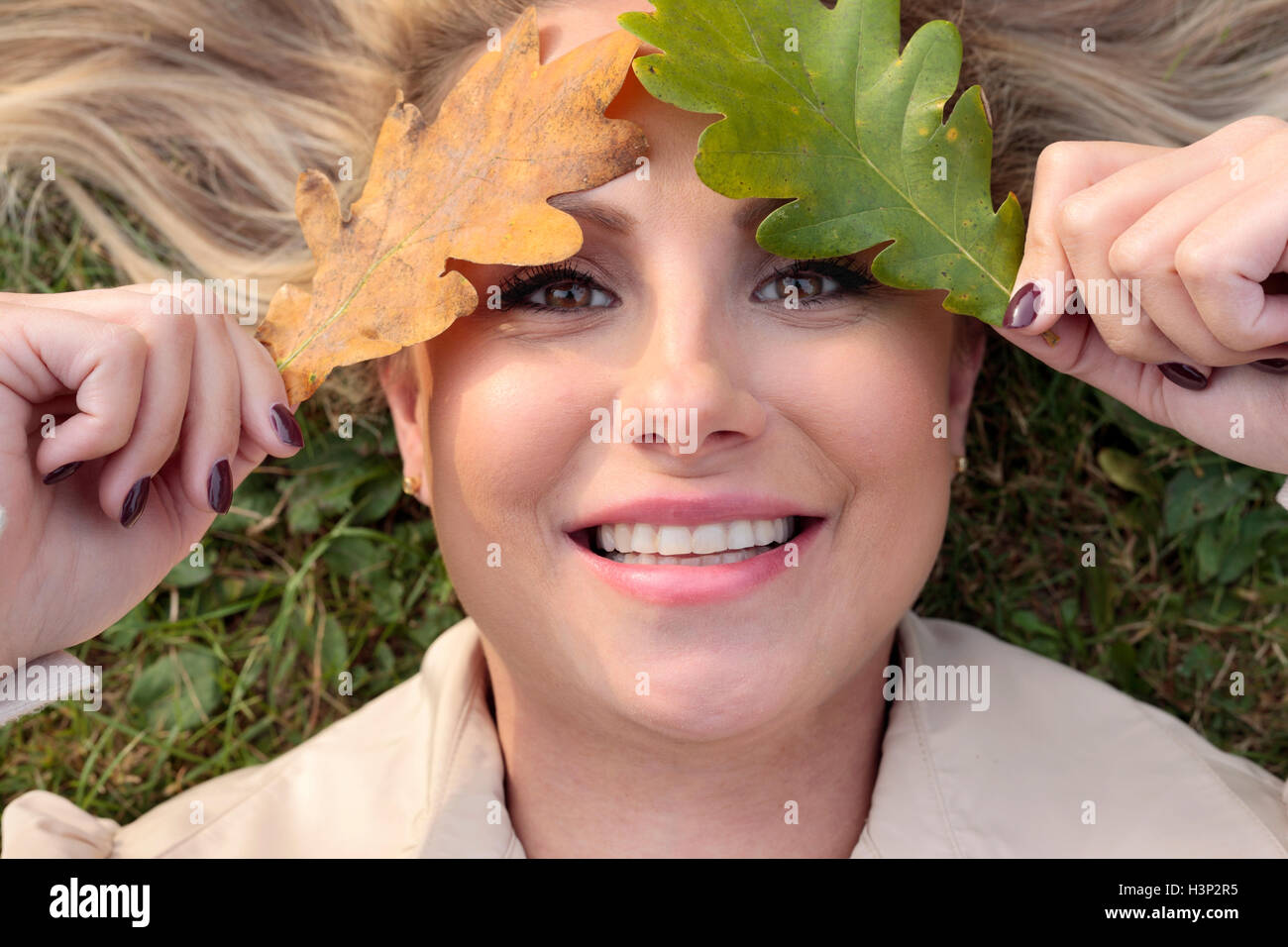 Woman lying on a meadow with her face covered with leaves Stock Photo