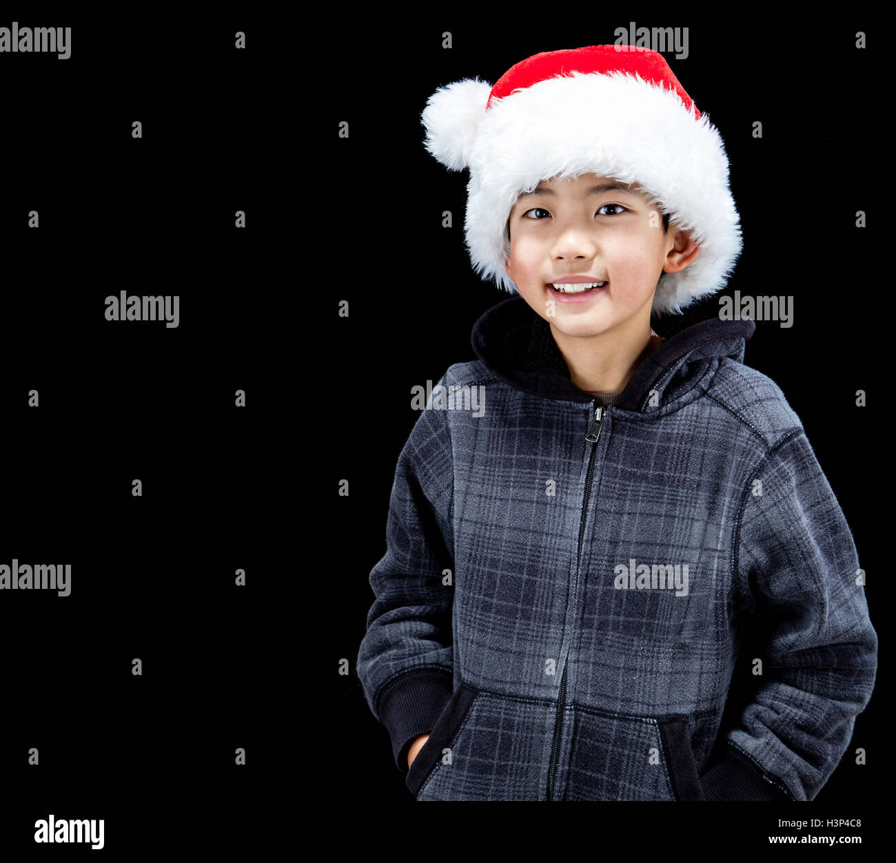 Cute Asian boy in Christmas mood wearing Santa Hat and fleece hoodie, isolated on black background. Copy Space. Stock Photo