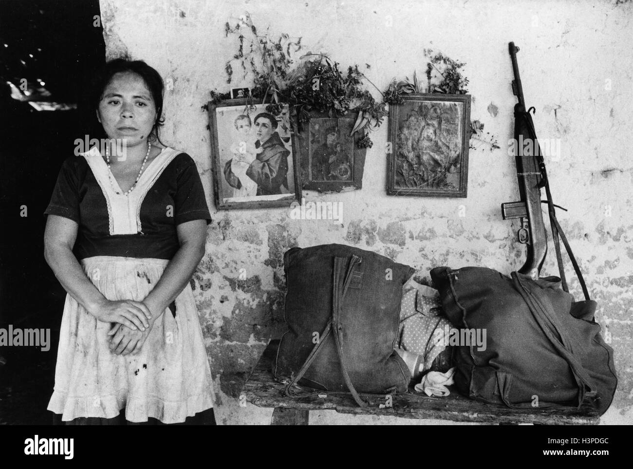CHALATENANGO,  EL SALVADOR, FEB 1984: - Within the FPL Guerrilla's Zones of Control.  A shop-keeper outside her house.  The gun and bags belong to popular militia members passing through. Stock Photo