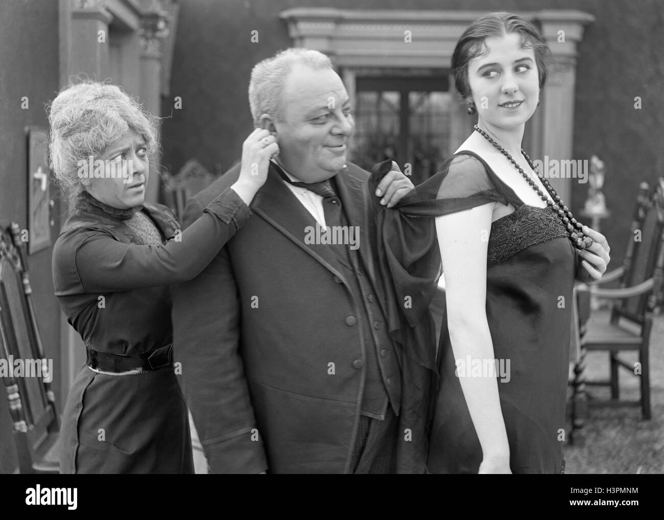 1910s 1920s OLDER SMILING MAN TUGGING ON YOUNG WOMAN’S DRESS WHILE WIFE TUGS ON MAN’S EAR SILENT MOVIE STILL Stock Photo