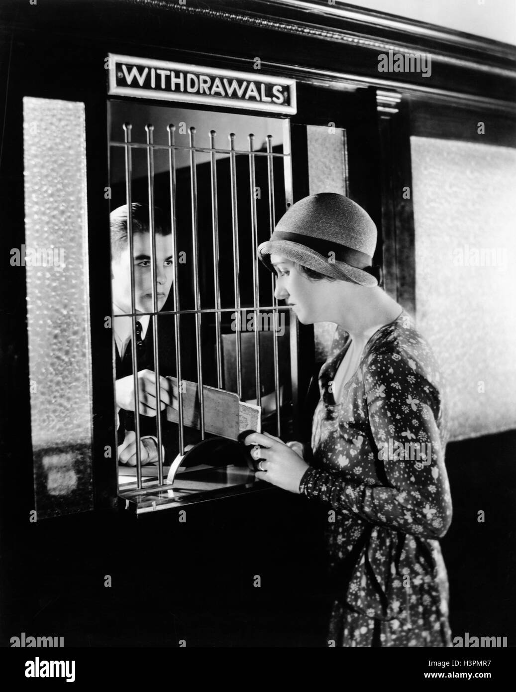 1920s 1930s WOMAN MAKING A CASH WITHDRAWAL FROM MALE BANK TELLER Stock Photo