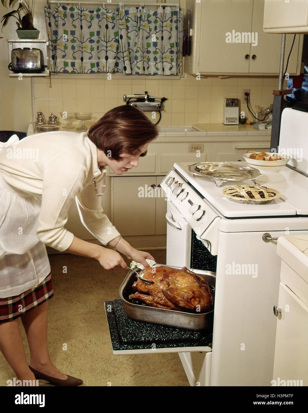 1950s WOMAN HOUSEWIFE BASTING THANKSGIVING ROAST TURKEY IN OVEN Stock Photo
