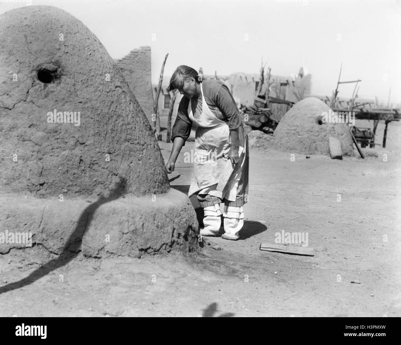 1930s NATIVE AMERICAN INDIAN WOMAN BAKING BREAD IN OUTDOOR HORNO OVEN SANTA CLARA PUEBLO NEW MEXICO USA Stock Photo