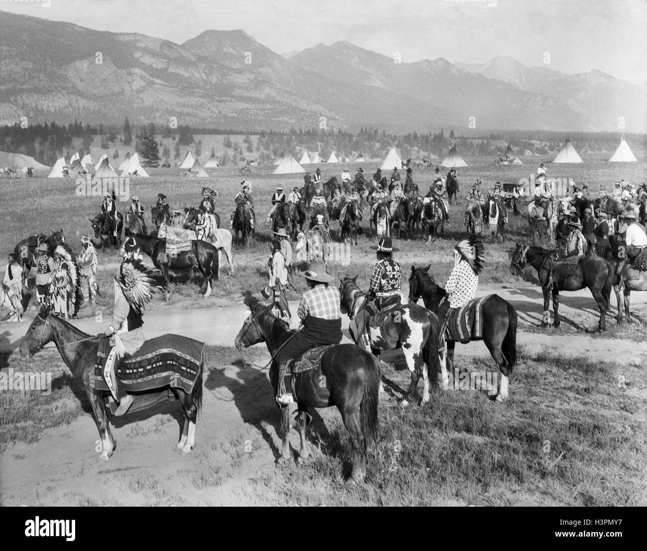 1920s LARGE GROUP OF NATIVE AMERICAN BLACKFOOT INDIANS MEETING BY VILLAGE ON HORSEBACK BRITISH COLUMBIA CANADA Stock Photo