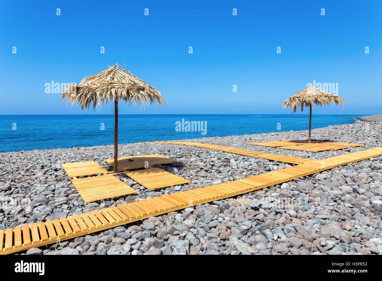Parasols with wooden path and stones at blue ocean on island Madeira Stock Photo