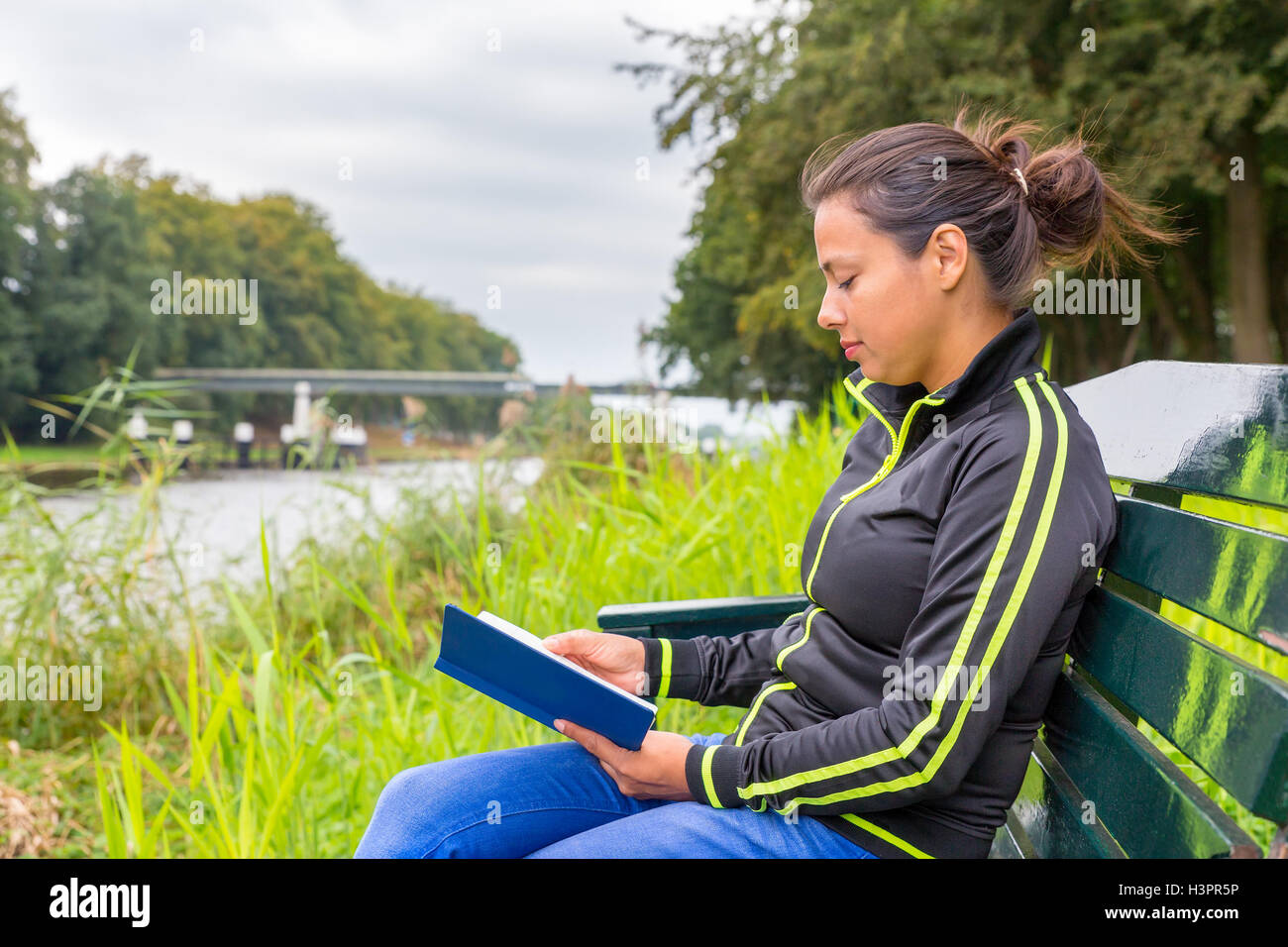 european woman on wooden bench at river reading book Stock Photo