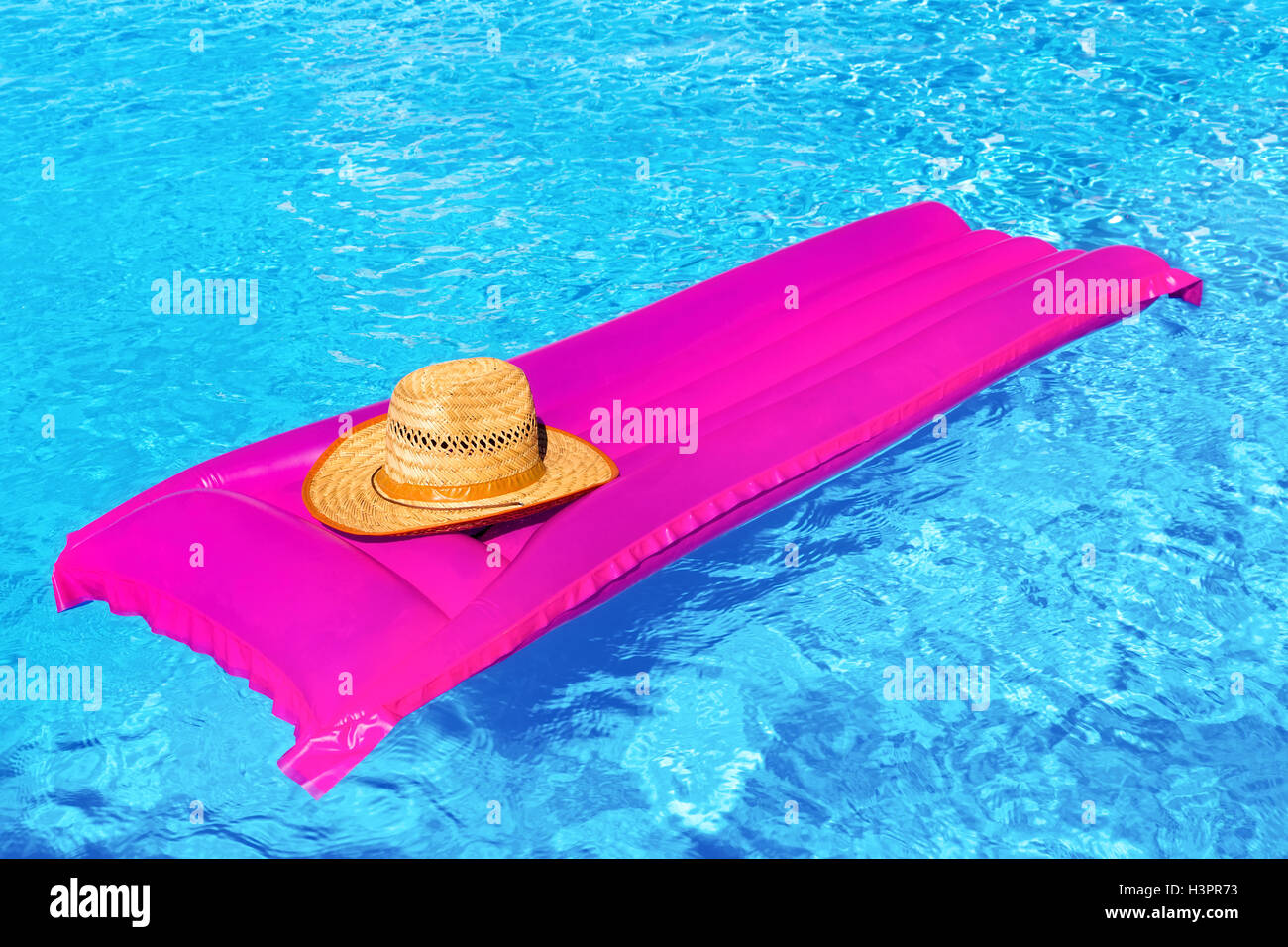 Pink air bed with straw hat in blue swimming pool Stock Photo