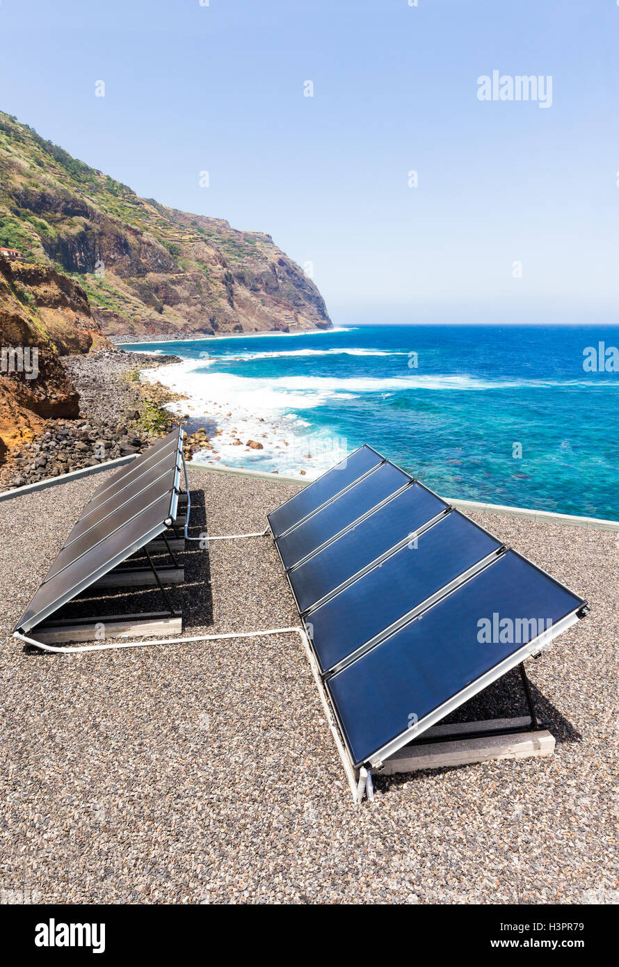 Rows of blue solar panels on house near beach, sea and mountain Stock Photo