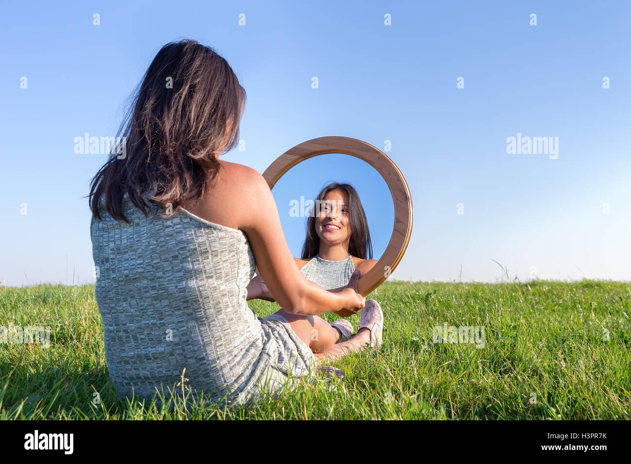 Woman sitting on grass looking at  her mirror image Stock Photo