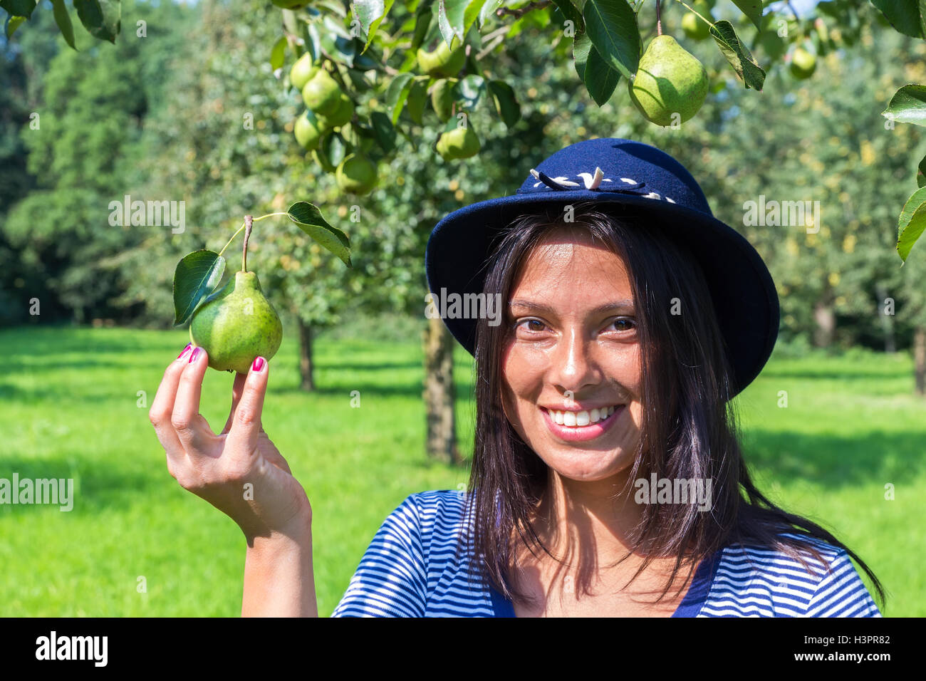 European woman wearing blue hat holding pear in orchard Stock Photo