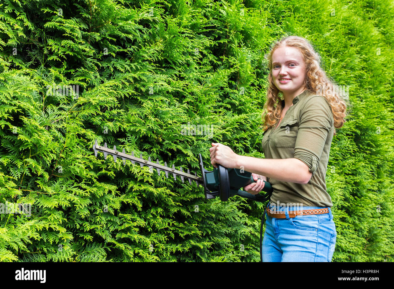 Young caucasian woman holding hedge trimmer at green conifers Stock Photo