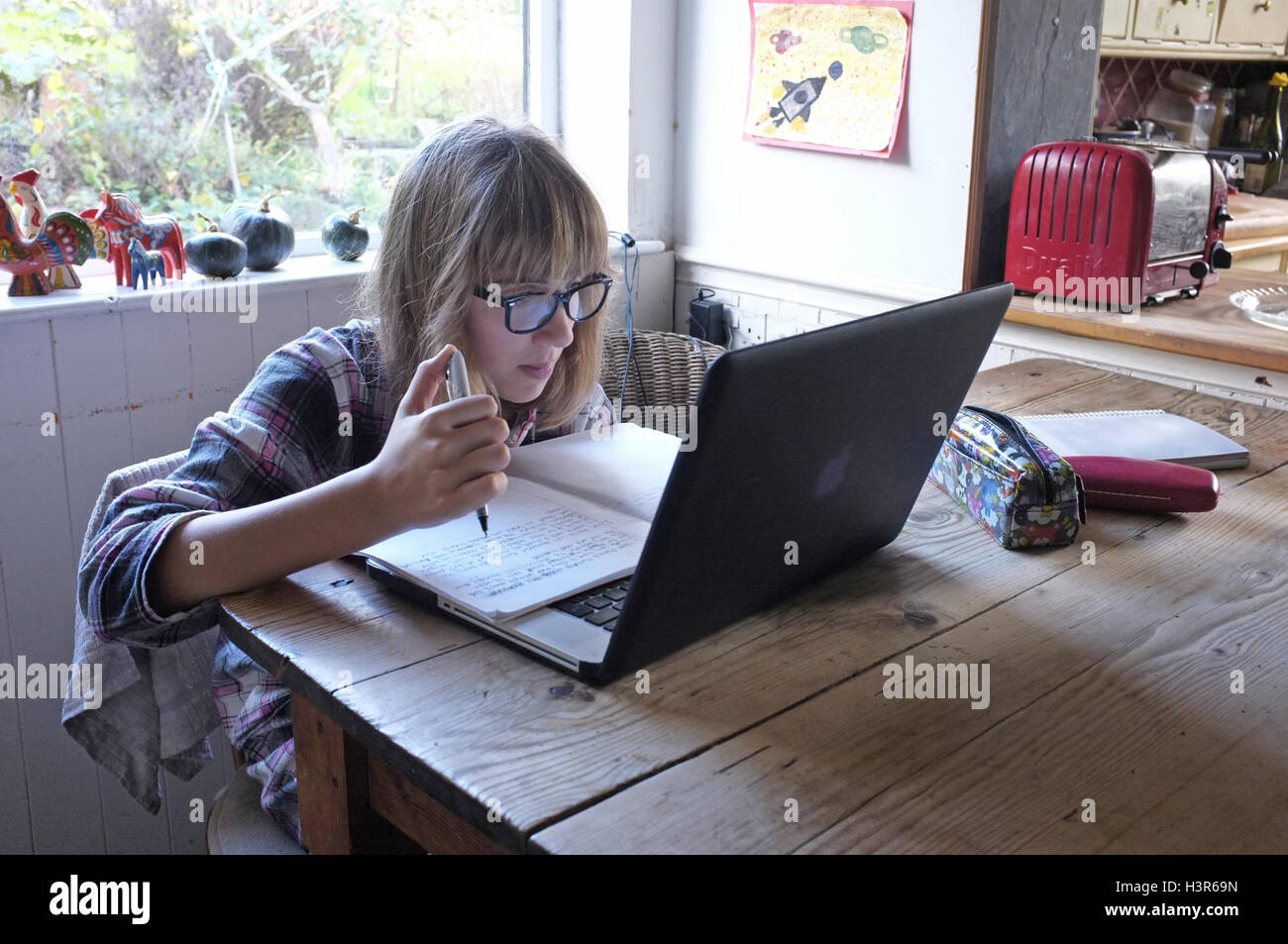 A 13 year old girl doing her homework on the kitchen table with her pajamas on. Stock Photo