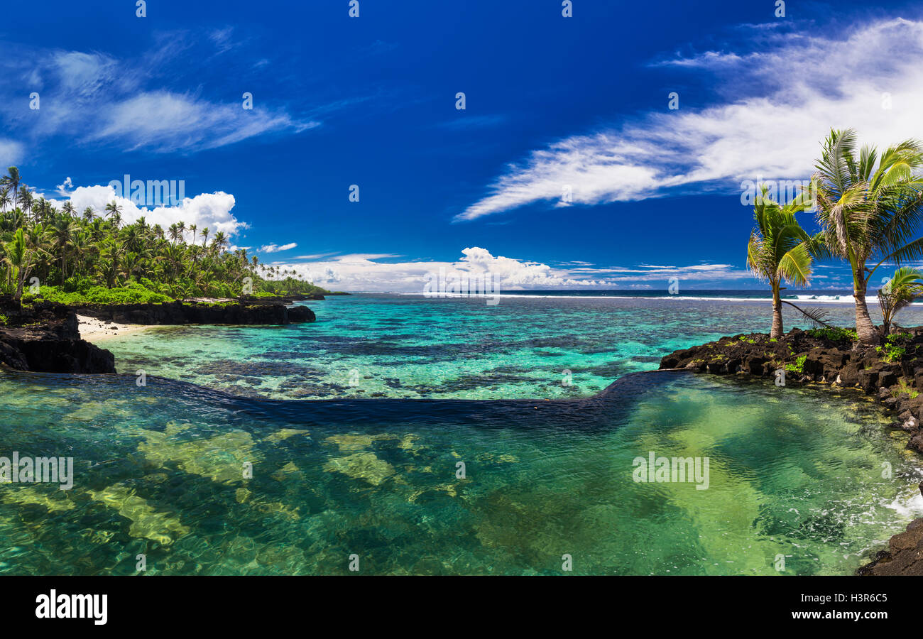 Natural infinity rock pool with palm trees over tropical ocean lagoon Stock Photo