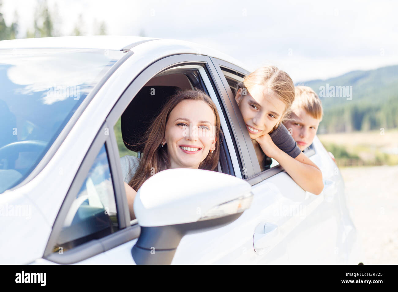 Happy young woman and her children sitting in a car and look out from  windows. Family travel background image Stock Photo - Alamy